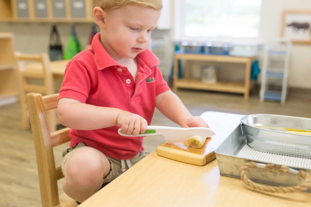 Child slicing a banana using a safe Montessori knife — a hands-on practical life activity