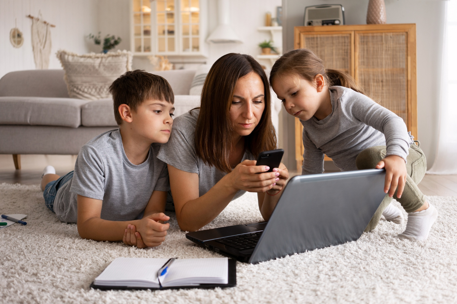 Mom guiding two kids through screen use with phone and laptop — healthy tech habits at home (raising kids in the digital age)
