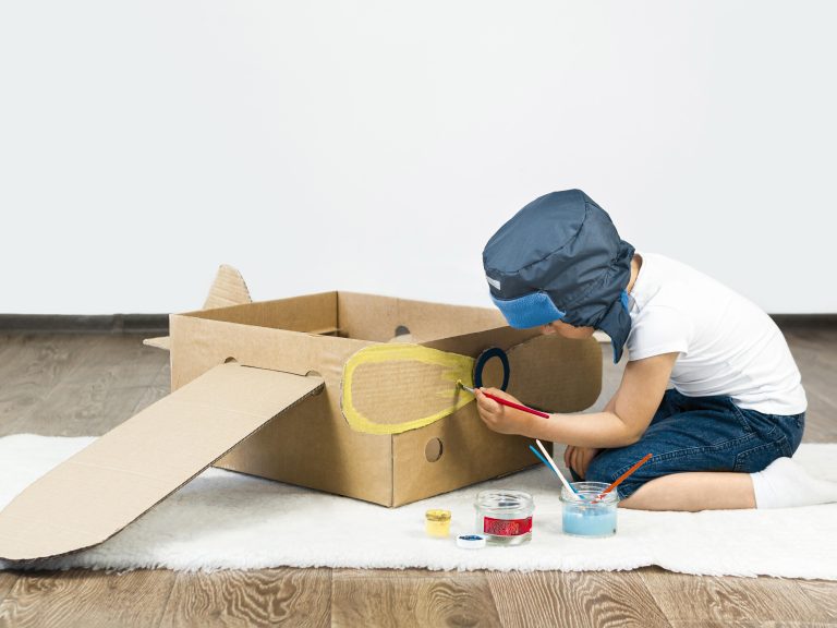 What is STEM for kids? A young child explores STEM concepts by building and painting a cardboard airplane using hands-on, screen-free materials at home